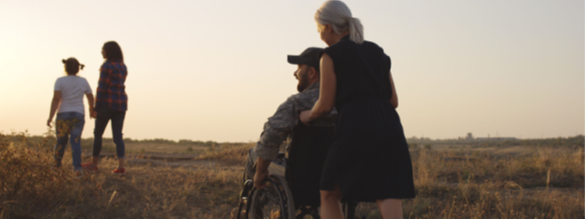 woman pushing man in a wheelchair outside